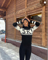 Person wearing a black and white striped sweater with 'SK' logo in front of a wooden building.
Perfect Moment á Íslandi - sælar.is