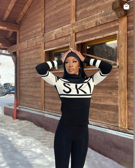 Person wearing a black and white striped sweater with 'SK' logo in front of a wooden building.
Perfect Moment á Íslandi - sælar.is