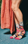 Person wearing colorful patterned socks with a towel draped over one leg on a blue surface. Xpooos sokkar - bestu sokkarnir - sætir sokkar