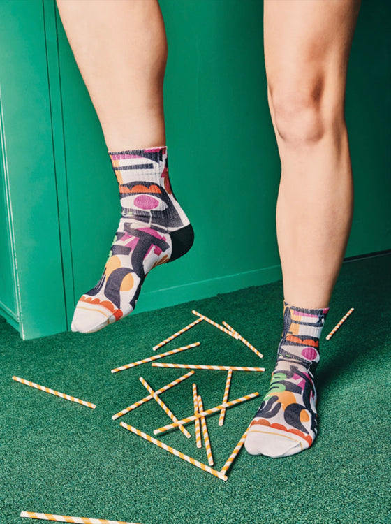 Person wearing colorful socks with a green background and scattered straws on the floor.
Sælar sokkar Xpooos - hringekja - bestu sokkarnir - sætir sokkar