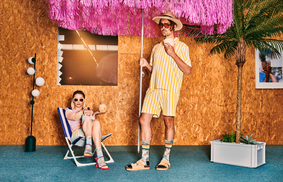Two people in a retro-themed room with a pink fringe umbrella and striped chairs.
Sælar sokkar Xpooos - hringekja - bestu sokkarnir - sætir sokkar
