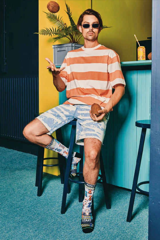 Person sitting on a stool wearing a striped shirt and shorts in a colorful room.
A pair of socks with a racing car design, featuring various cars with a start and finish line.
Sælar - sokkar Xpooos - bestu sokkarnir - sætir sokkar