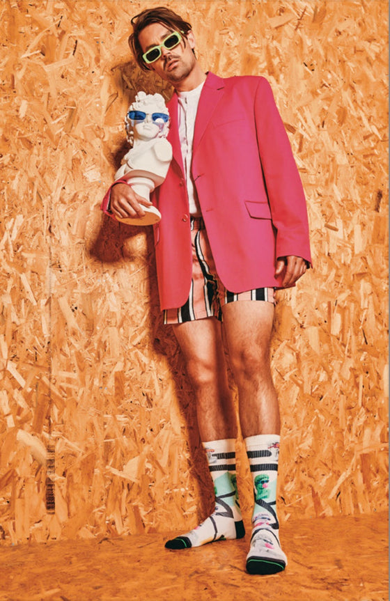 Person wearing a pink blazer and colorful socks holding a dog figurine against a wooden panel background
Sælar - sokkar Xpooos - bestu sokkarnir - sætir sokkar